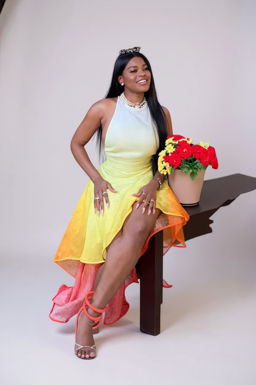 Woman in a colorful dress sitting on a chair with flowers, on a plain background