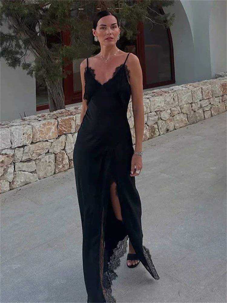 Woman in a black dress standing outdoors with stone wall and tree in the background