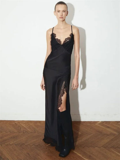 Woman wearing a black lace dress standing against a white wall.