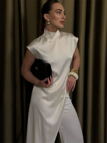 Woman in a white dress holding a black clutch against a brown curtain background