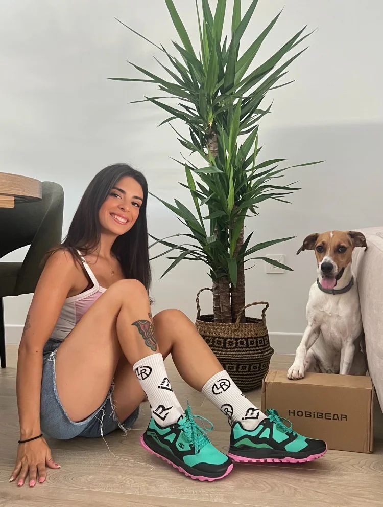 Woman sitting on the floor wearing colorful sneakers with a dog and plant in the background
