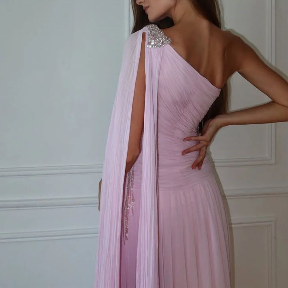 Woman wearing a pink one-shoulder dress with a decorative embellishment against a white wall.