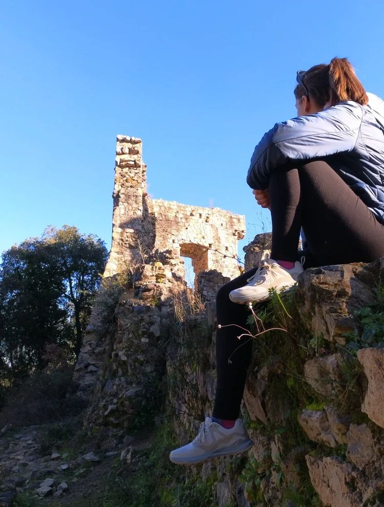 Two people sitting on a stone wall overlooking an ancient ruin with a clear blue sky.