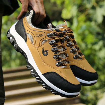 Tan and black hiking shoes with 'Zuodi' branding held by a person against a blurred green background.