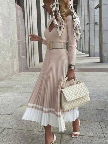 Woman in a stylish outfit with a pleated dress, scarf, and handbag walking outdoors.