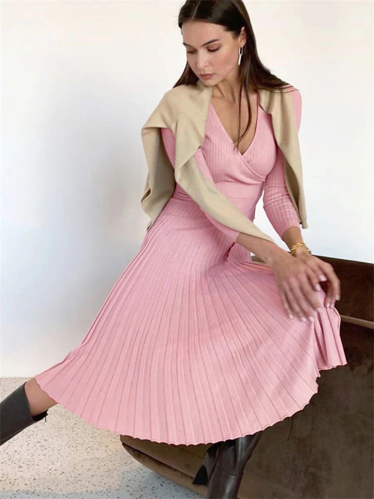 Woman wearing a pink pleated dress with a beige cardigan against a white background
