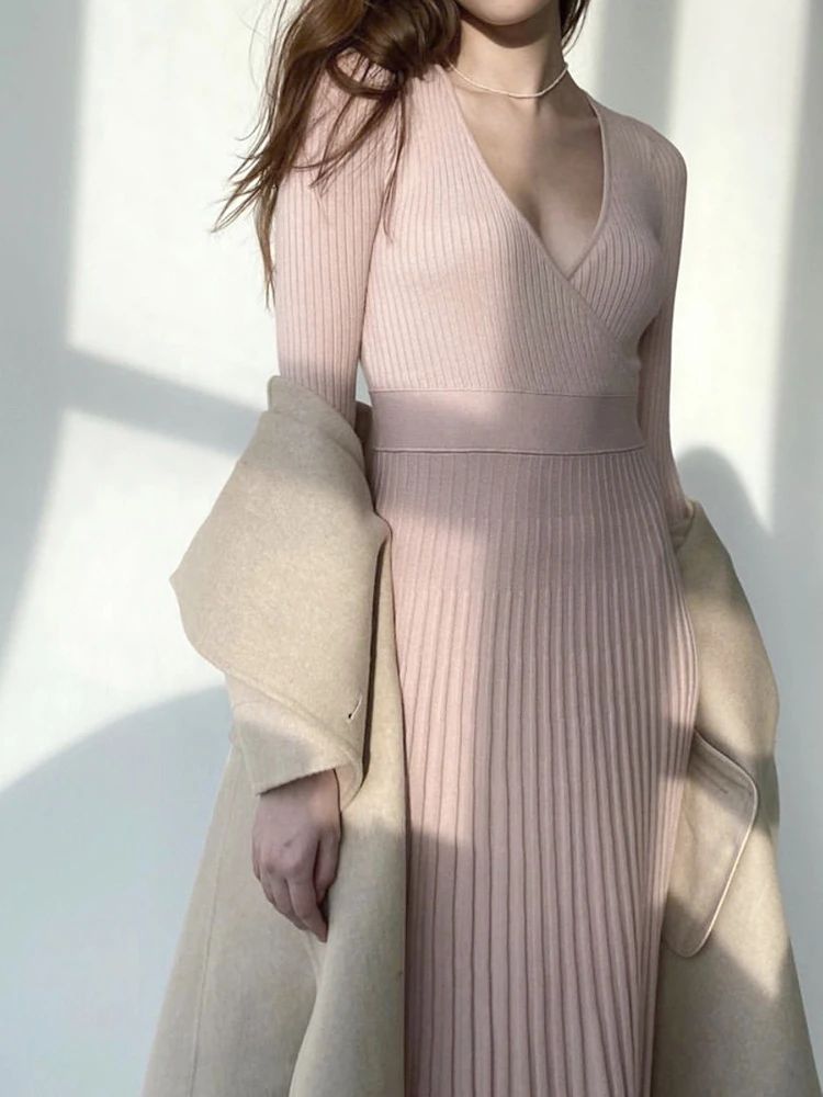 Woman wearing a light pink ribbed dress with a beige coat against a white background