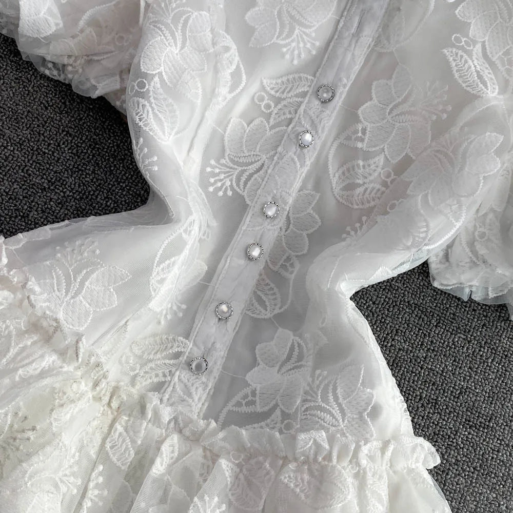 Close-up of a white lace garment with floral patterns and small embellishments on a dark surface.