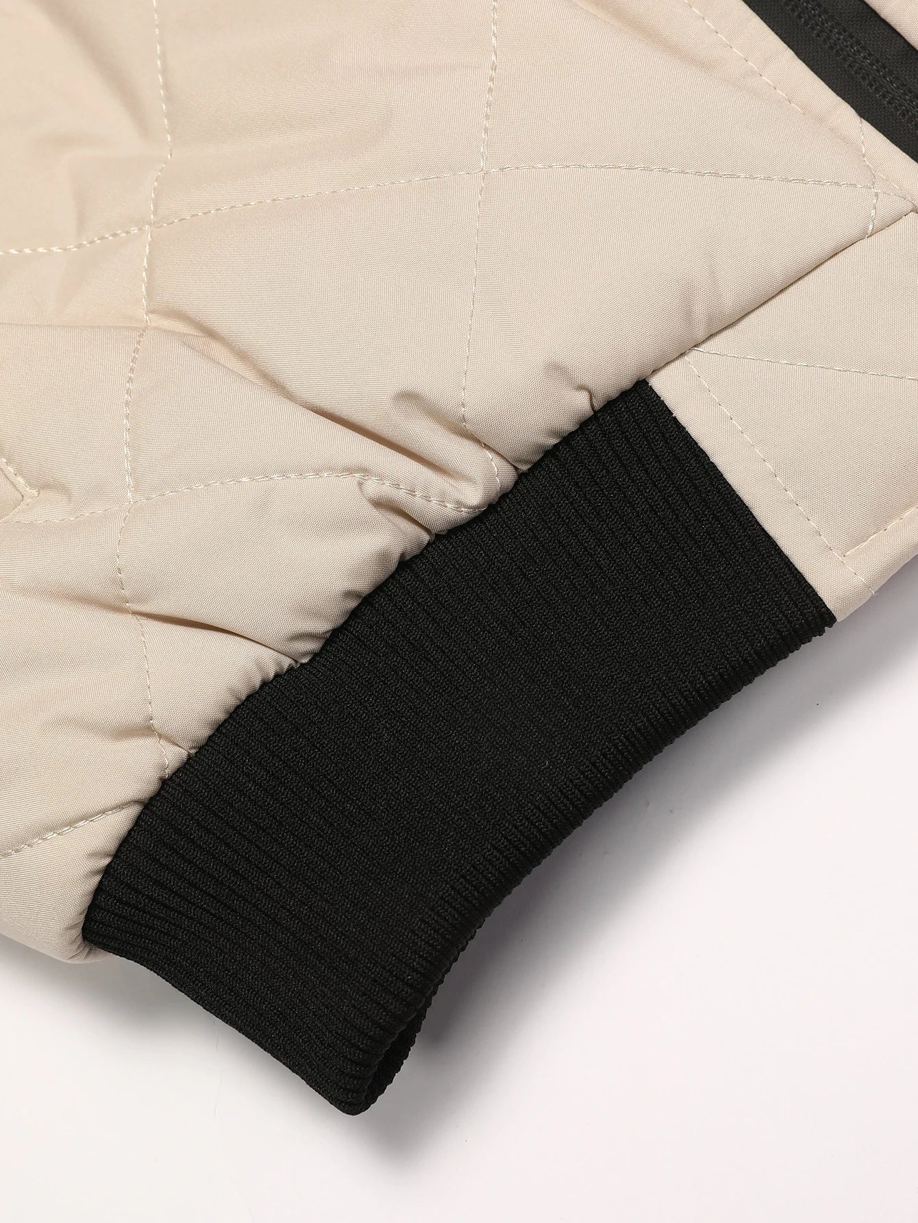 Close-up of a beige quilted jacket with black ribbed cuffs on a white background