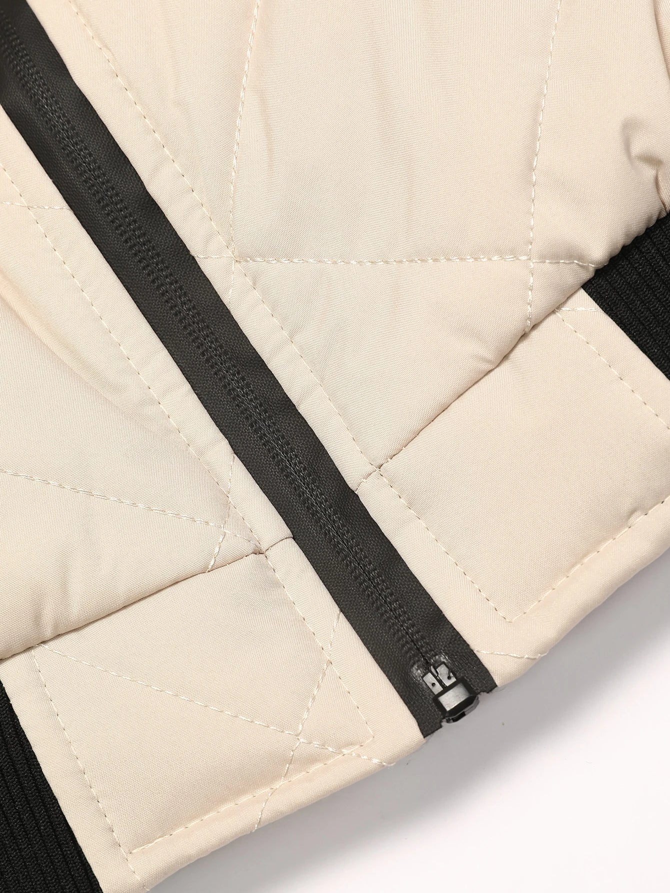Close-up of a beige quilted jacket with a black zipper on a light gray background