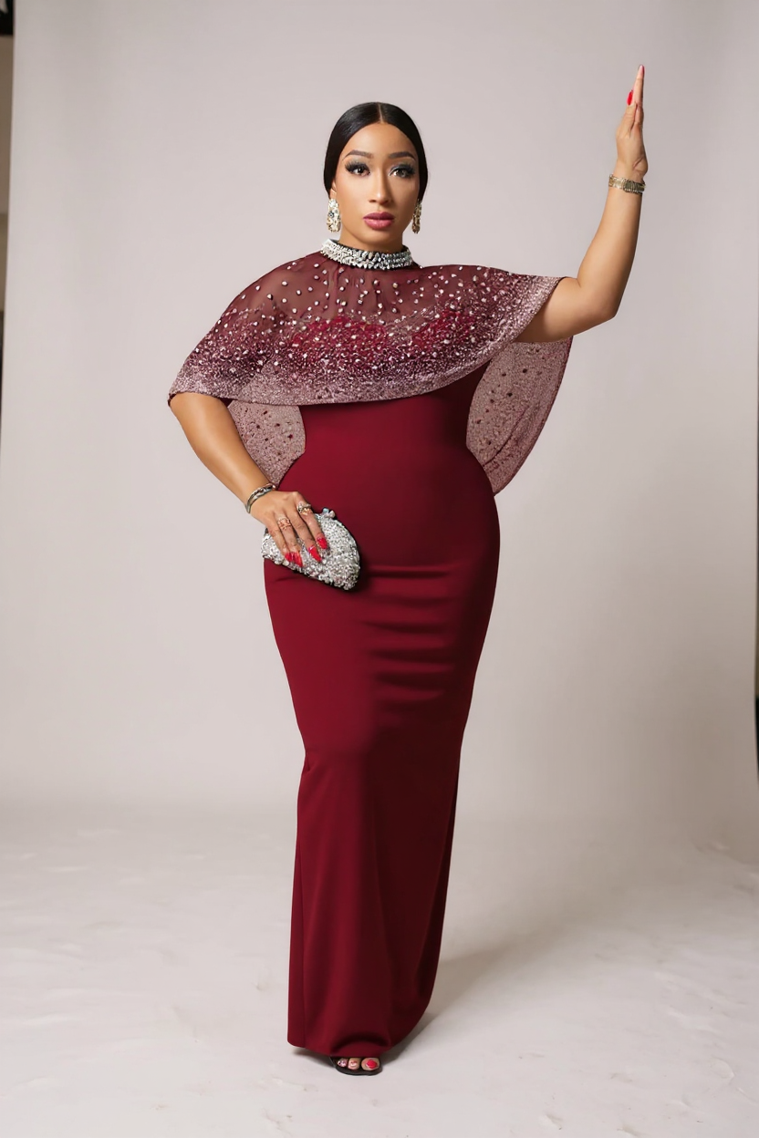 Woman in a burgundy dress with a sparkling cape against a plain background
